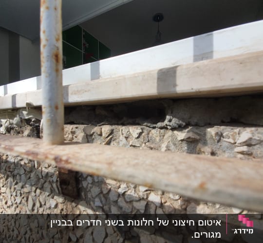 סדק בקיר אבן מתחת לחלון עם מסגרת מתכת חלודה